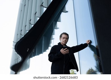 Man checking his smartphone while leaning against a modern building in daylight