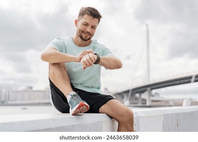 Man checking his smartwatch, wearing a dark shirt and black shorts, against a cloudy sky. - Powered by Shutterstock