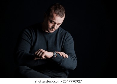 Man checking his watch while seated in a dimly lit environment.
