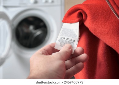 A man checking  information the label on a red sports jacket, with a washing machine in the background. Clothes care and washing rules. Selective focus. - Powered by Shutterstock