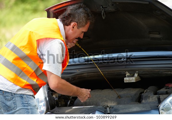 Man\
checking level of oil on a car engine\
dipstick