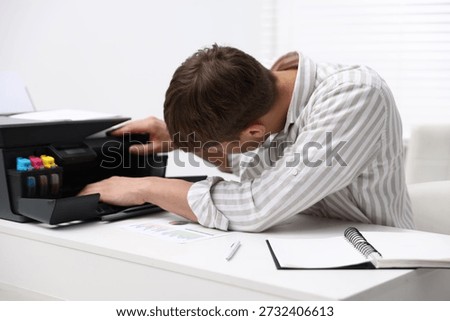 Man checking printer ink levels at white desk in office