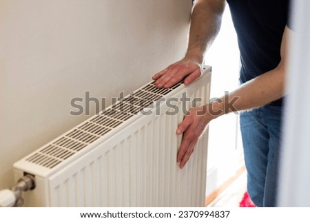 Man is checking radiator is it heating. Man warming his hands on the radiator. Home central heating system. 