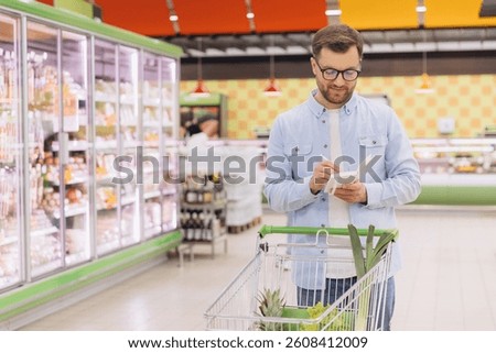 Man checking shopping list while pushing trolley in grocery store