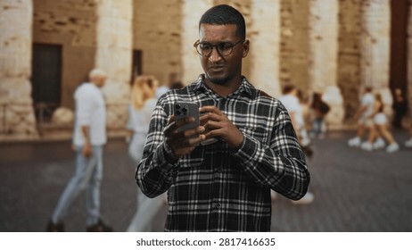 Man checking smartphone while holding a coffee cup on a historic street with stone columns and passersby; concern focus.