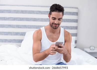 Man checking smartphone while sitting on bed in bedroom with bedside table and analog alarm clock. Minimalist, relaxation, technology, comfort, modern, cozy, leisure
