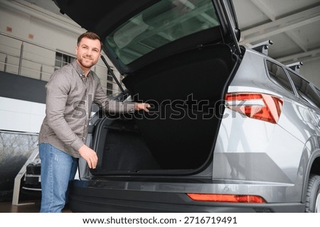 Man checking the trunk space of a new suv in a car dealership, considering cargo capacity before purchase
