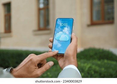 Man checking weather using app on smartphone outdoors, closeup. Data and illustration of cloud on screen
