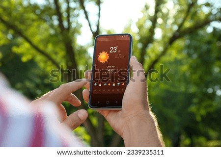 Man checking weather using app on smartphone outdoors, closeup. Data, sun and other illustrations on screen
