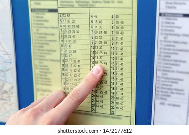 Man checking a yellow bus timetable pointing his finger at the hour of bus arrival. Public transportation, travelling by train or a bus, arriving on time or late concept, punctuality