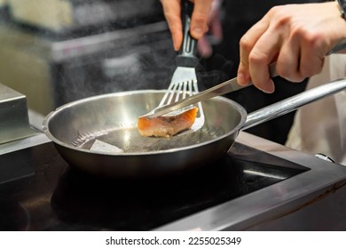 man chef cooking fried salmon fish in frying pan on kitchen - Shutterstock ID 2255025349