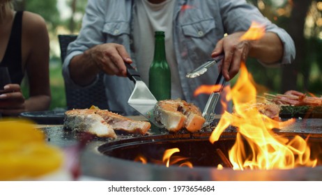 Man Chef Finishing Cooking Outside. Unknown Guy Taking Part In Fish Preparation On Backyard. Unrecognizable Man Using Tongues And Spatula Outdoors. Man Hands Grilling In Summer Forest.