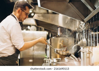 Man chef frying meat in a pan in fire - Powered by Shutterstock