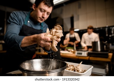 man chef holds handful of oyster mushrooms in his hands from which drops of water flow down into bowl on kitchen