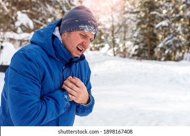 Man with chest pain suffering from heart attack while standing in snowy nature during the day. Shot of a Caucasian man holding chest in pain outdoors.  Man holding chest while suffering with heartburn