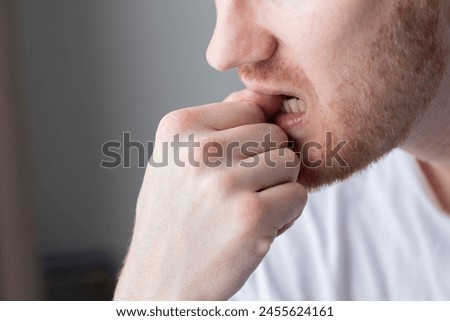 A man chewing on his fingernails with a worried expression. Closeup.