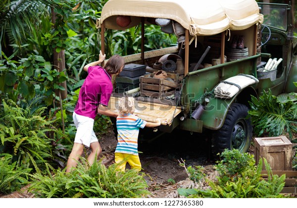 Man and child push car stuck in mud in\
jungle. Family pushing off road vehicle stuck in muddy dirt terrain\
in tropical forest. Island adventure\
drive.