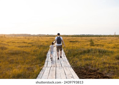 Man with child  walking in wildlife national park at sunset. Wooden boardwalk through swamp in late summer. Concept of ecotourism, hiking, vacation, travel with children. Selective focus. - Powered by Shutterstock