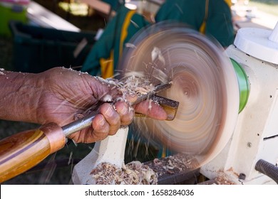 Man With A Chisel Turning A Wooden Bowl On A Wood Lathe With Shavings Flying Off The Work As It Spins.