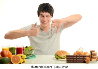 Man Choosing Between Fruits, Smoothie And Organic Healthy Food Against Sweets, Sugar, Lots Of Candies And A Big Hamburger, Unhealthy Food