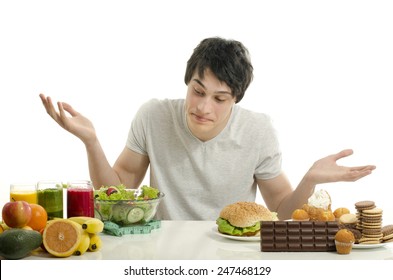 Man Choosing Between Fruits, Smoothie And Organic Healthy Food Against Sweets, Sugar, Lots Of Candies And A Big Hamburger, Fast Food