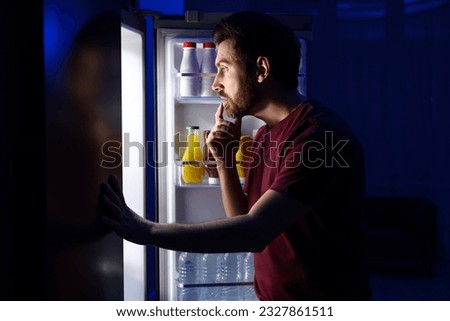 Man choosing food from refrigerator in kitchen at night. Bad habit