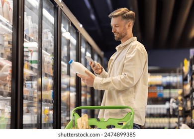 Man choosing fresh dairy products in supermarket, holding bottle and mobile phone, scanning bar code on product and checking information - Powered by Shutterstock