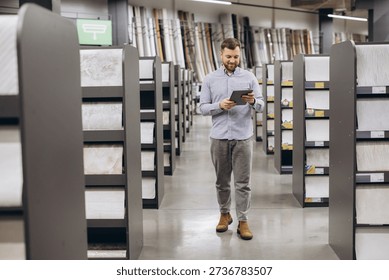 Man choosing materials for interior design project in a hardware store aisle, navigating options on a tablet