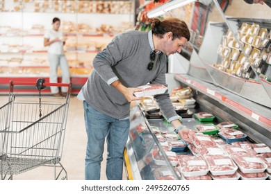 Man choosing packaged raw sausages in supermarket - Powered by Shutterstock