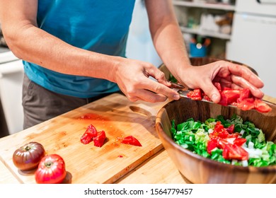 Man Chopping Vegetables On Cutting Board Table In Kitchen Placing Juicy Red Heirloom Tomatoes With Vibrant Color From Garden Into Salad Wooden Bowl