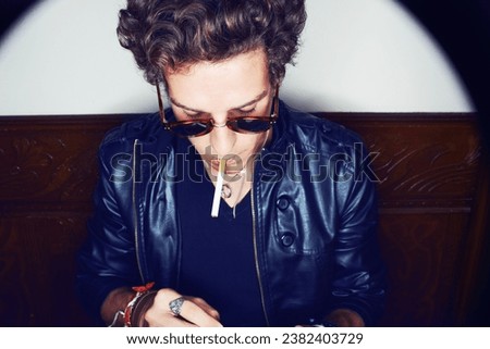 Man with cigarette, punk in sunglasses and rockstar attitude on white background with spotlight. Cool rock style, grunge fashion and smoking, confident and handsome male model in studio with freedom.