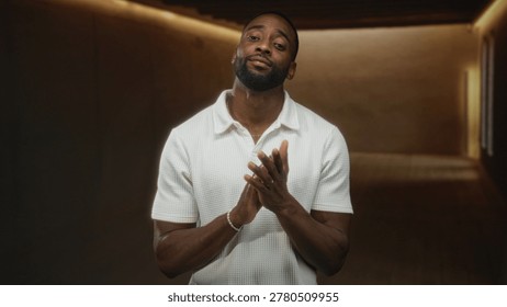 Man clapping hands in studio wearing white polo shirt and gold necklace under warm lighting; confidence focus poise.