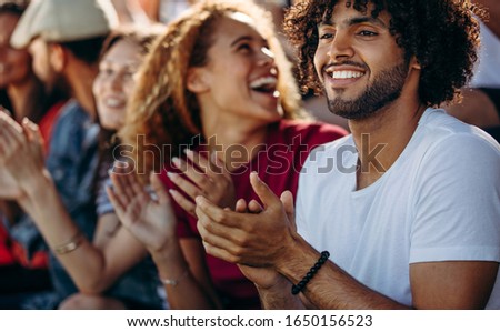 Man clapping while watching a soccer match with friends at stadium. Multi-ethnic group of friends enjoying watching a football game at stadium.