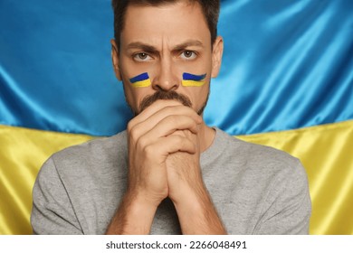 Man with clasped hands near Ukrainian flag, closeup - Powered by Shutterstock