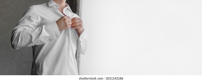 A man clasps buttons on a white shirt with his hands in the light from the window. - Powered by Shutterstock