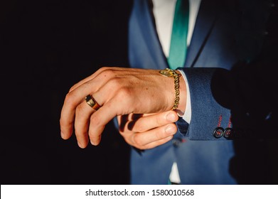 A Man Clasps A Gold Bracelet On His Arm. Hands Of Successful Businessman In Tuxedo, Closeup. Men's Accessories, Bracelet And Gold Ring On A Man's Hand.