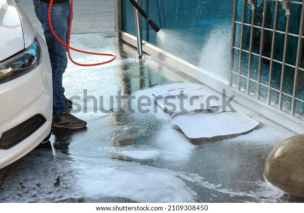 Man cleaning auto mats with high pressure\
foam jet at self-service car wash,\
closeup
