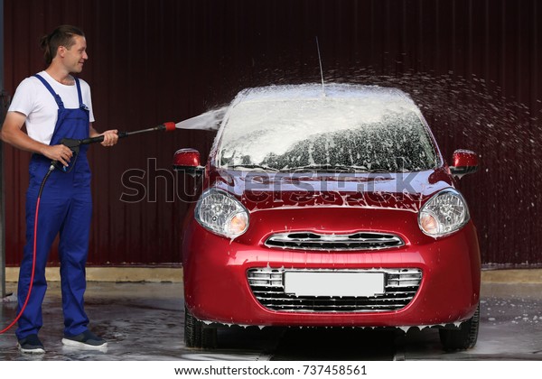 Man cleaning automobile with high pressure water at\
car wash