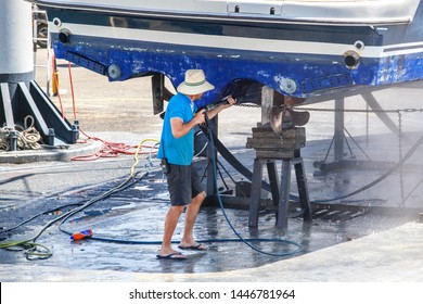 Man cleaning boat with high pressure water.  A man on a dock with a pressure cleaner working on  pontoon boat.