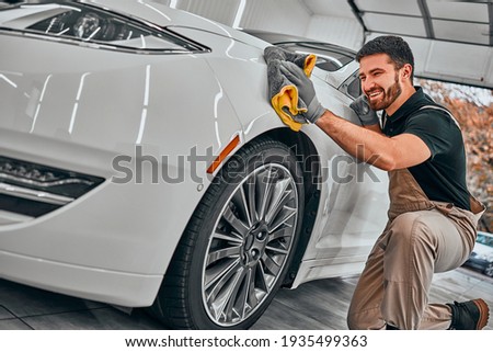 Man cleaning car and drying vehicle with microfiber cloth. Hand wipe down paint surface of shiny white car after polishing and ceramic coating. Car detailing and car wash concept. Selective fiocus.