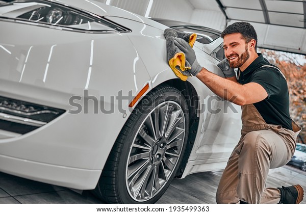 Man cleaning car and drying vehicle with\
microfiber cloth. Hand wipe down paint surface of shiny white car\
after polishing and ceramic coating. Car detailing and car wash\
concept. Selective fiocus.