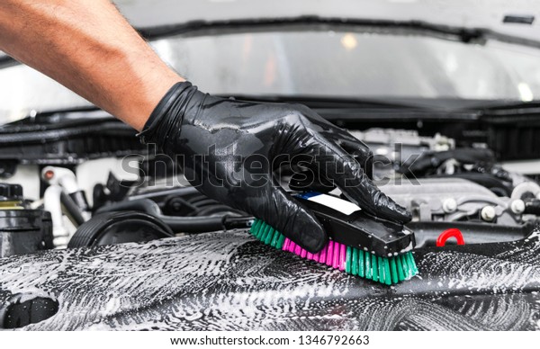 A man cleaning car engine with shampoo and brush.\
Car detailing or valeting concept. Selective focus. Car detailing.\
Cleaning with sponge. Worker cleaning. Car wash concept solution to\
clean