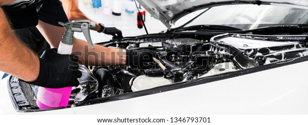 A man cleaning car engine with shampoo and brush.\
Car detailing or valeting concept. Selective focus. Car detailing.\
Cleaning with sponge. Worker cleaning. Car wash concept solution to\
clean
