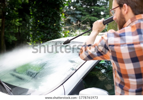 Man cleaning a car in the garden with a compact high\
pressure washer .