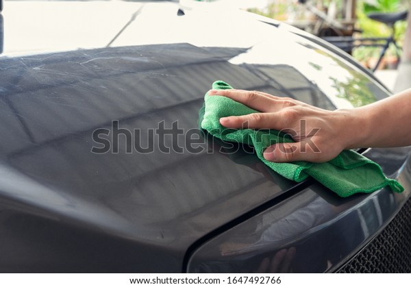 Man\
cleaning car with green microfiber cloth on car\
hood