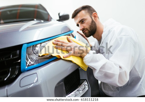 A man cleaning car with microfiber cloth, car\
detailing (or valeting) concept. Front lights protected with\
isolation blue tape. Selective focus.\
