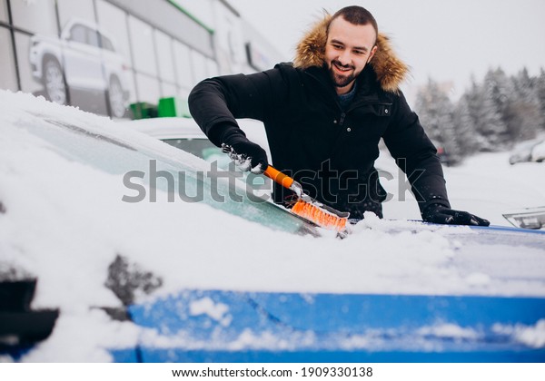 Man cleaning car from\
snow with brush