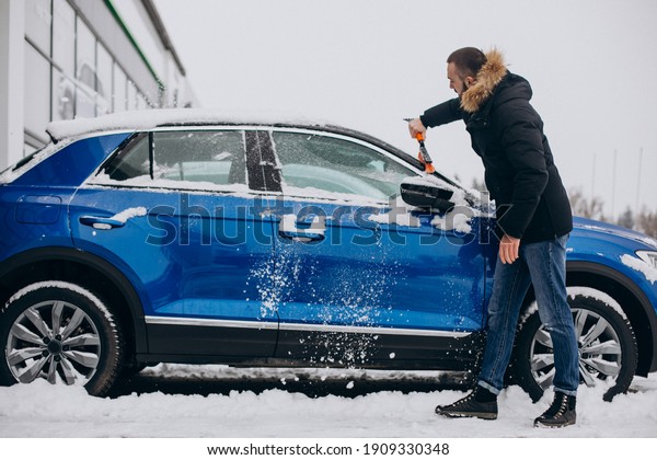 Man cleaning car from\
snow with brush