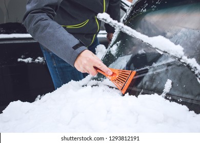 Man Cleaning Car From Snow And Ice With Brush And Scraper Tool During Snowfall. Winter Emergency. Weather-related Vehicle Emergencies. Automobile Covered With Snow