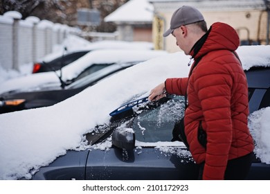 Man Cleaning Car From Snow And Ice With Brush And Scraper Tool During Snowfall. Winter Emergency. Weather-related Vehicle Emergencies. Automobile Covered With Snow